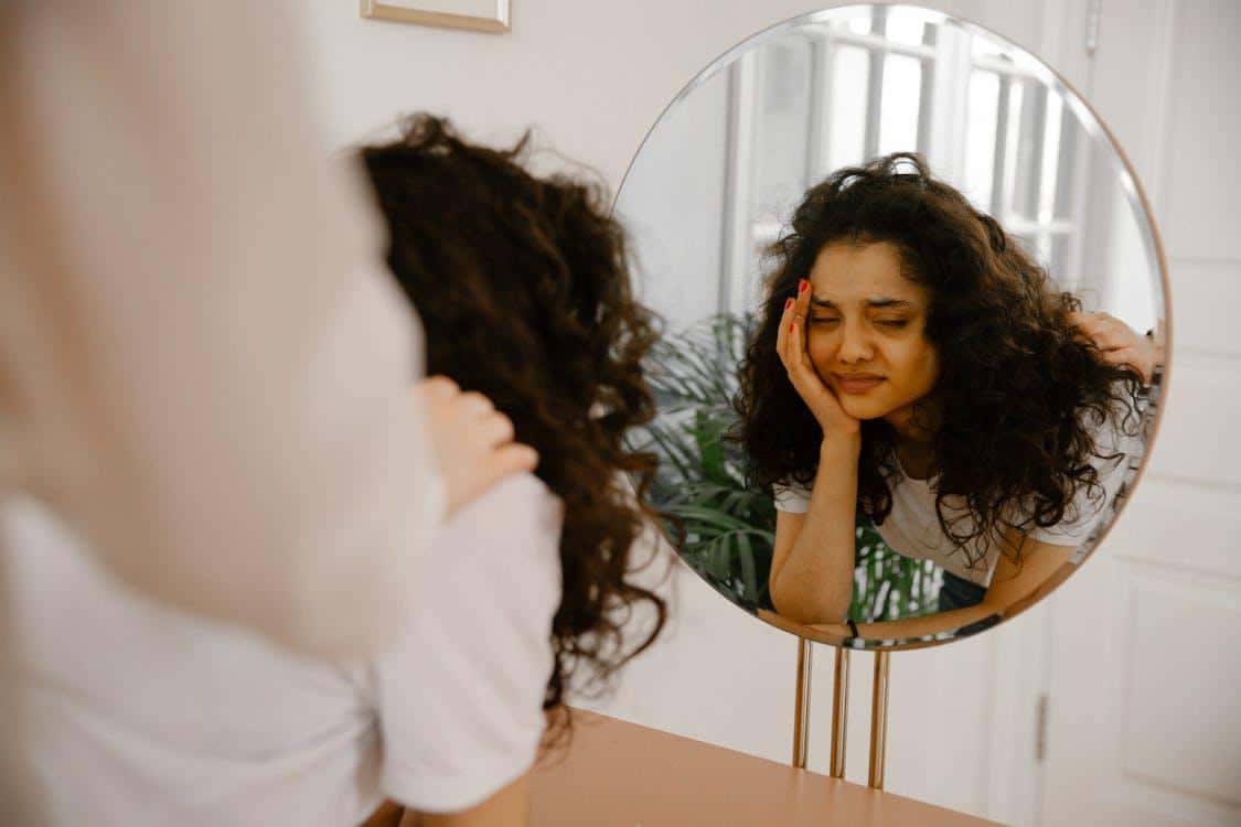 Young woman looking at herself in a mirror, appearing emotionally distressed, showing mood instability