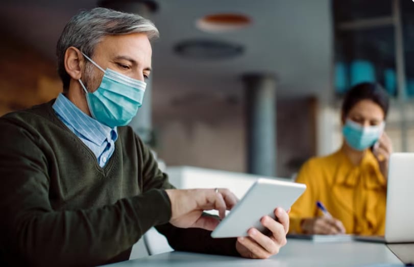 Male entrepreneur wearing face mask using digital tablet while working and checking FMLA eligibility