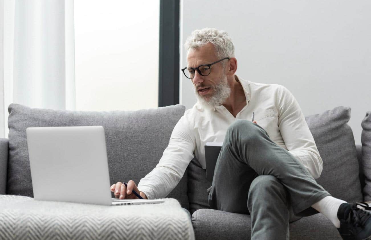 A senior man using a laptop while reviewing medical leave paperwork.