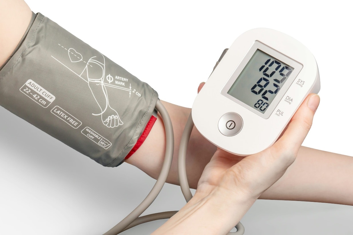 Person checking blood pressure at home using a digital monitor showing an elevated reading