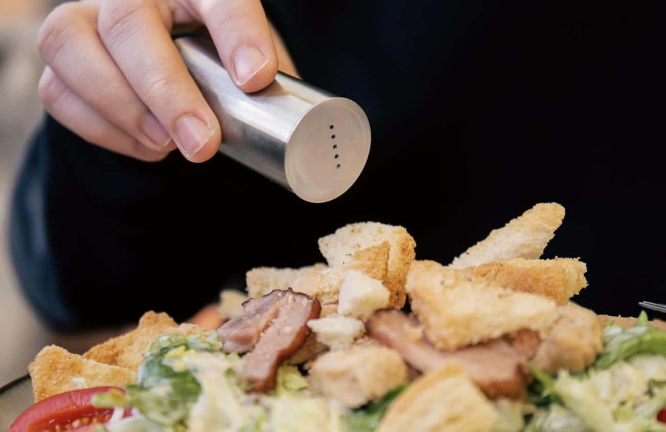 A person seasoning a salad with salt.
