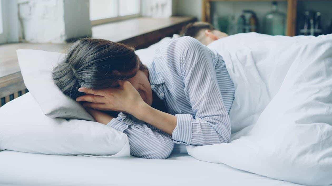 Woman lying in bed covering her face, showing depressive episode and fatigue linked to bipolar disorder
