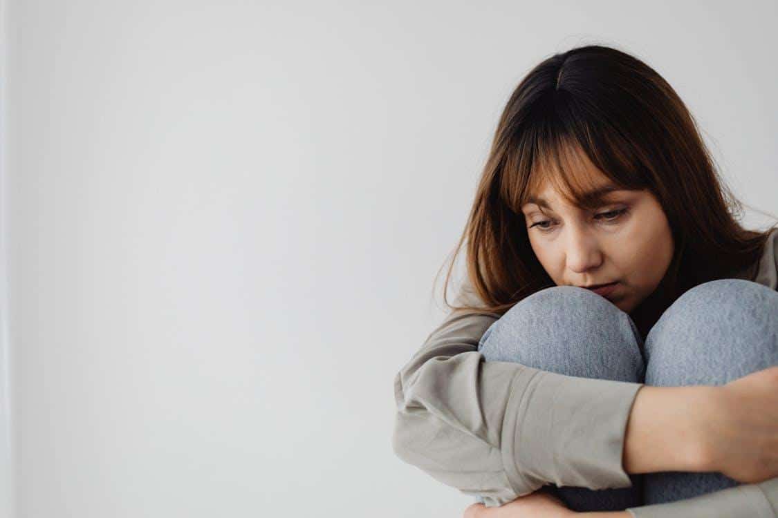a woman hugging her knees and looking upset.