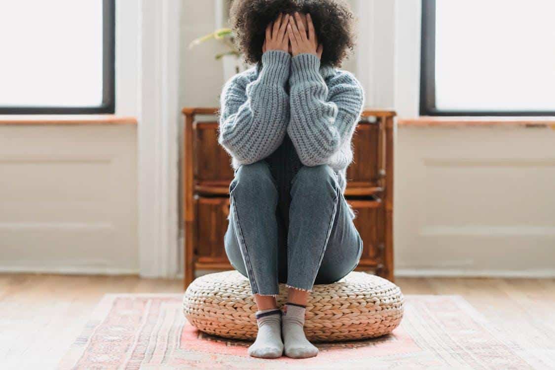 a woman sitting on the floor and hiding her face in her hands.