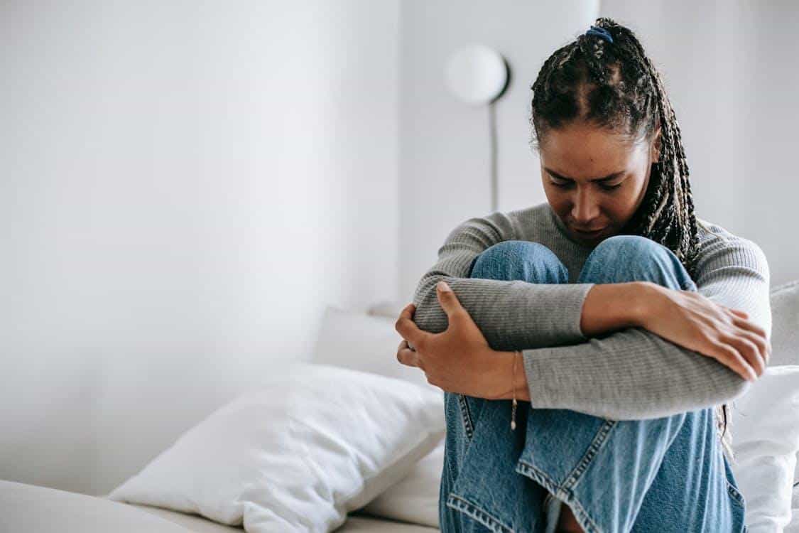 a woman sitting on her bed and looking upset.